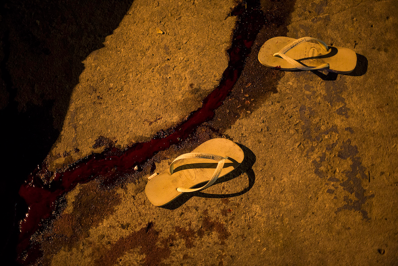 “A pair of flip-flops alongside a stream of blood from a homicide victim in Seropedica, in greater Rio de Janeiro, Brazil. The victim was a young, black man and according to people at the scene it was a gang-related shooting. Just the night before, 11 people were killed in separate incidents, the majority gang related.”